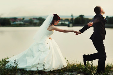 Groom runs along the lake's shore holding bride's hand tightly