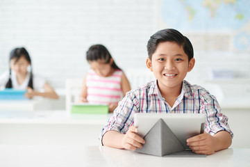 SMiling school kid with tablet computer sitting in class