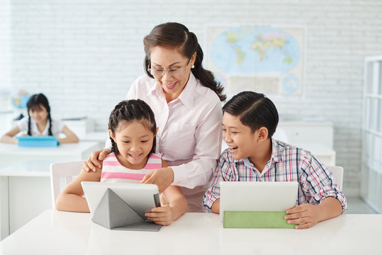 Laughing children and teacher using app on tablet computer