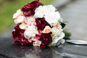 Bouquet of wine-colored and white flowers lies on a black car