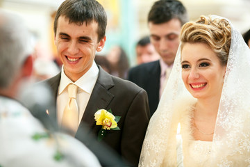 Beautiful newlyweds smile standing before a priest during the ce