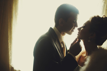 Groom holds bride's chin tender before a kiss standing in the ro