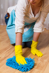 Wash wood floor concept. Young woman wipes the floor with a cloth gloves, sitting on his lap