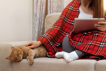 Girl covered by plaid sittingon the couch and looking at tablet.