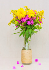 a bouquet of flowers of goldenrod, chrysanthemums, phlox in a glass vase on a gray background