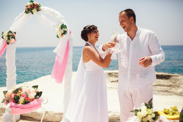 Adult bride and groom cross their hands to drink champagne by th