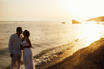 Bride leans to a groom standing on the bright sea shore while su