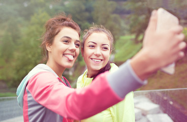 Two young women friends having fun in a park taking selfie with a smartphone. Active lifestyle and friendship concept