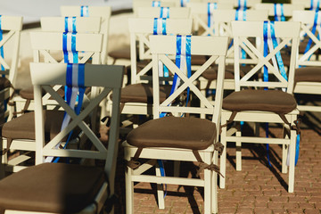 Beig chairs decorated with blue ribbons stand on the backyard