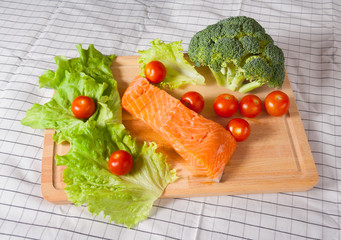 Fresh salmon with tomatoes, broccoli and salad on a cutting board