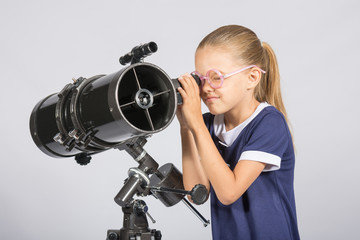 Seven-year girl in glasses with interest looks in a reflector telescope