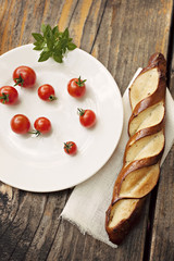 Cherry tomatoes with fresh basil and a bread bun on a wooden table. Copy space   