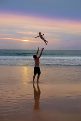 Fototapeta na wymiar Father throws his daugter at the beach near the sea at the spect