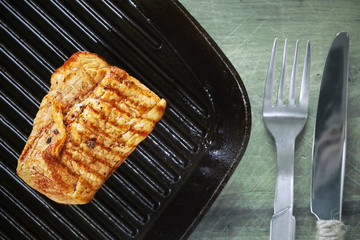 Close up picture of a roasted pork loin in black pan on wooden table.