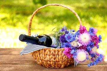 Fototapeta na wymiar Wine bottle with flowers in basket on table