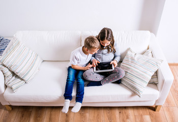 Children at home sitting on sofa, playing with tablet