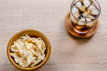 close up in dried squid and cola in glass on wooden background