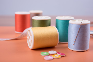 closeup needles, thread spool, scissors, button on wooden background.