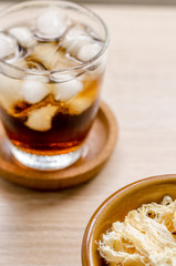 close up in dried squid and cola in glass on wooden background