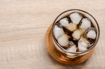 Glass of cola with ice on wooden background
