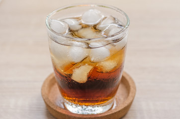 Glass of cola with ice on wooden background
