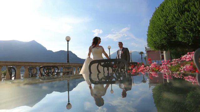 Happy bride and groom walk and hold hands on the park summer terrace. Como, Italy