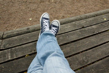 feet in blue sneakers and jeans on a wooden bench