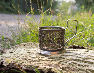 patterned silver stand for glasses,slightly covered with patina, stands on a piece of bark from the tree, near the grass, Sunny day