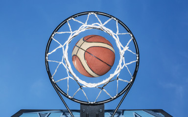 Basketball falling through the net. Blue sky on the background.