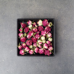 Dried rose in a square shape, over gray rusty background. Flat lay.