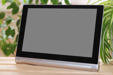 The tablet stands on wooden table on green background. Layout.