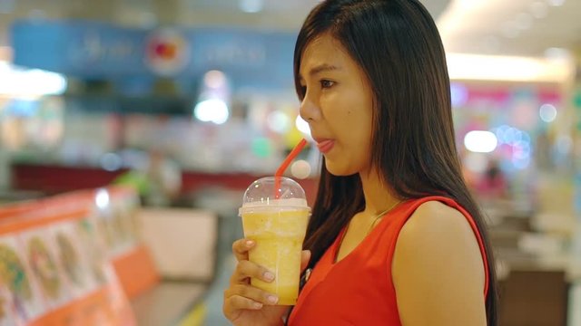 Young Asian Lady drinking orange shake in mall
