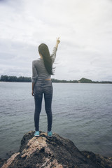 Woman standing on a cliff near the sea and looking to sea,gesturing two fingers,lifestyle outdoors,Beautiful inspirational landscape,activity concept,fighting and the winner concept,filtered image
