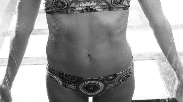 Closeup of womans stomach wearing bikini under outdoor shower - black and white video