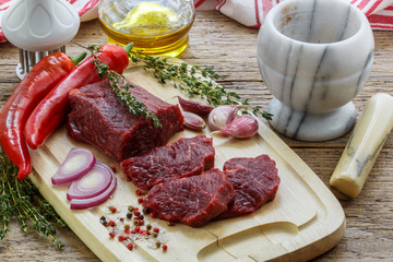 Beef. Fresh raw meat on a cutting Board, olive oil, garlic, hot pepper, thyme and spices on the table
