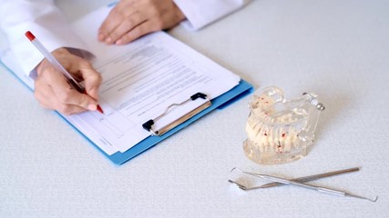 Medical assistant writing and signing dental checklist sitting at the table with dentist tools. Healthcare and medicine concept. 