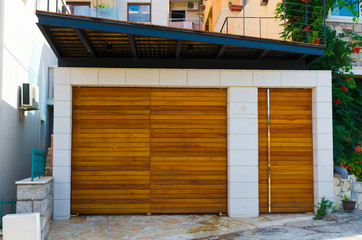 Brown wooden gates in garage in summer sunny day with white wall.