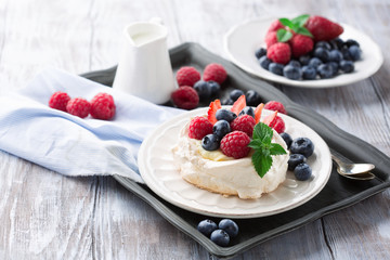 Meringues Pavlova cakes with fresh raspberry and blueberry on dark rustic wooden background, selective focus
