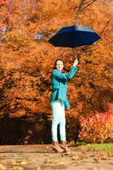Girl walking with blue umbrella in autumnal park