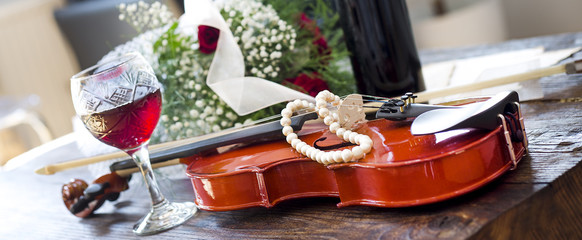 Violin, wine, red roses and music notes on wooden table 