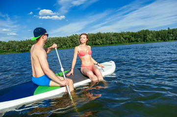 сheerful young couple sitting on the board stand up paddle boar