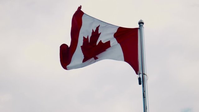 Canadian flag flying from a flagpole in a wind against a cloudy blue sky in a patriotic image