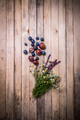 berries plums scattered on the wooden surface with a bouquet of daisies and a sprig of sage