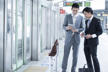 Two young businessman looking at the tablet at the station
