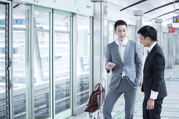 Two young businessmen have a stand talking at the station