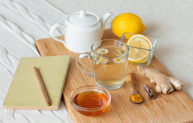 Herbal tea in glass cup with flowers of chamomile, turmeric and honey on a wooden board. Treatment with a cold drink. Treatment of folk remedies in bed. Book reading