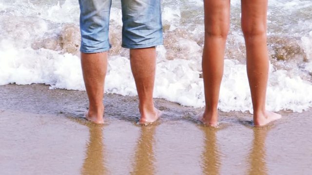 Slow motion.  Female and man  legs  on   summer sea coast among waves

