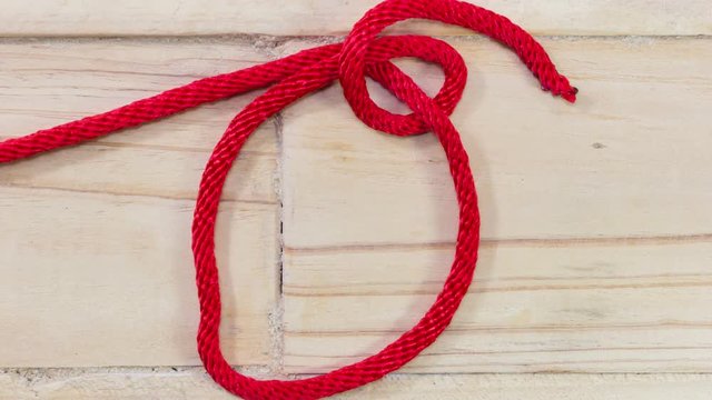 4k stop motion tarbuck knot made with red rope on wooden background.