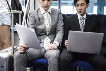 Two young businessmen are working on a train