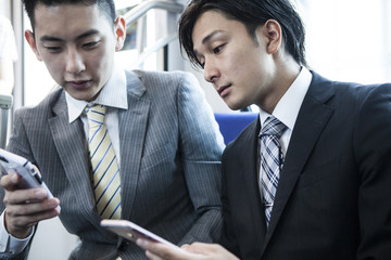 Two young businessmen have become addicted to smart phone on a train